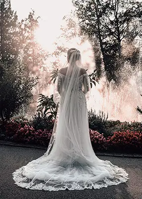 Braut mit langem weißem Schleier vor hell erleuchtetem Springbrunnen beim Fotoshooting